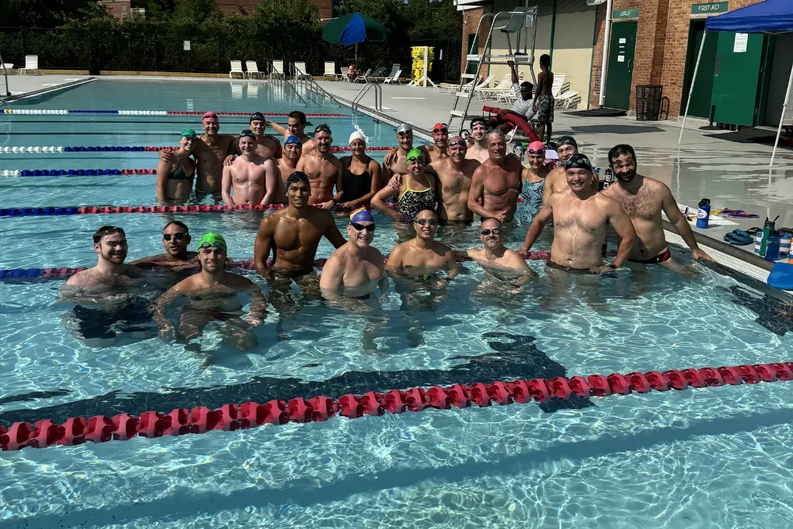 About thirty DCAC swimmers in caps and goggles gathered in the shallow end of an outdoor pool.